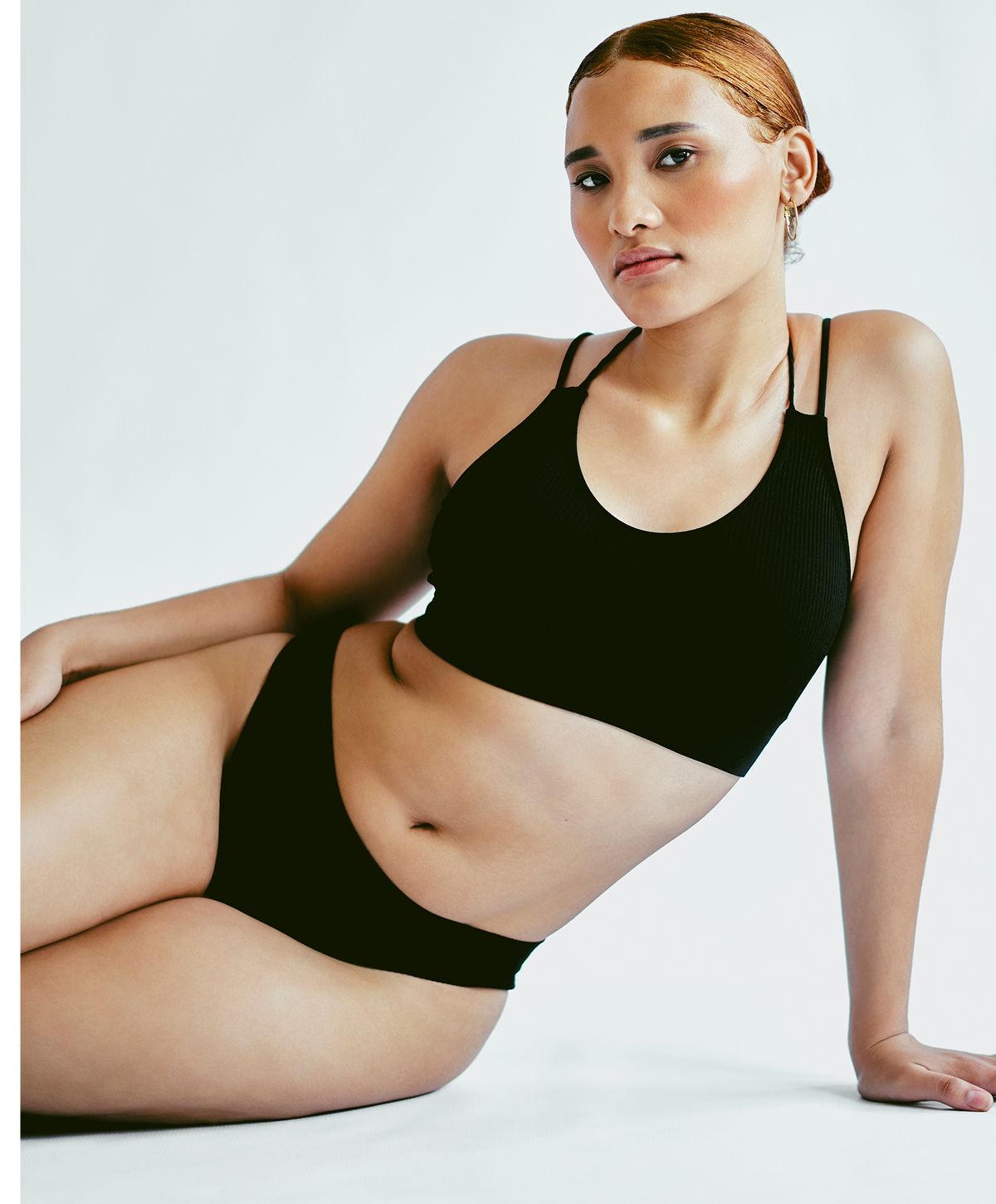 Model posing in black bikini against white background.