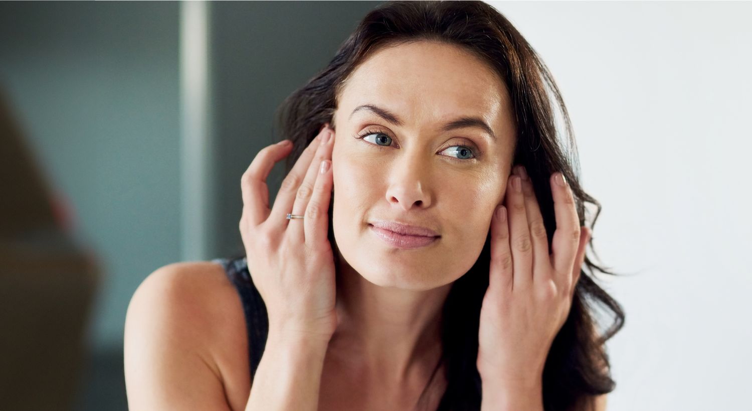 Woman touching her face in mirror reflection.