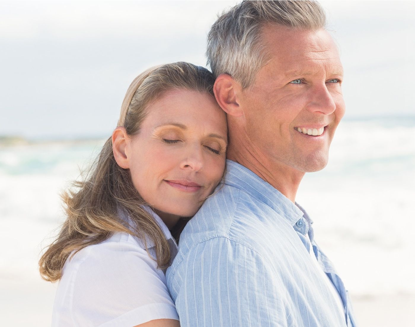 Couple embracing on the beach, smiling happily.