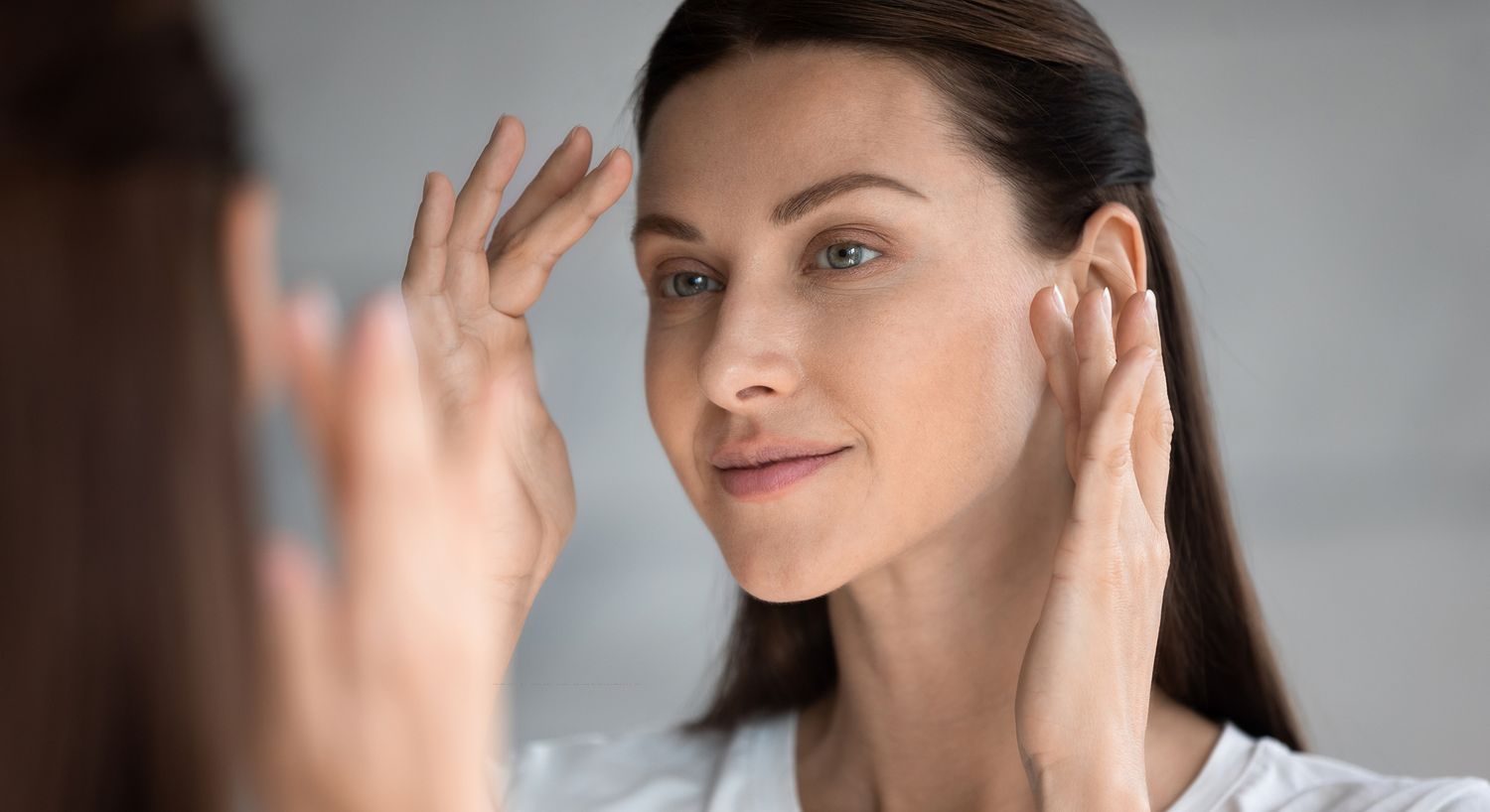 Woman applying skincare in front of mirror.