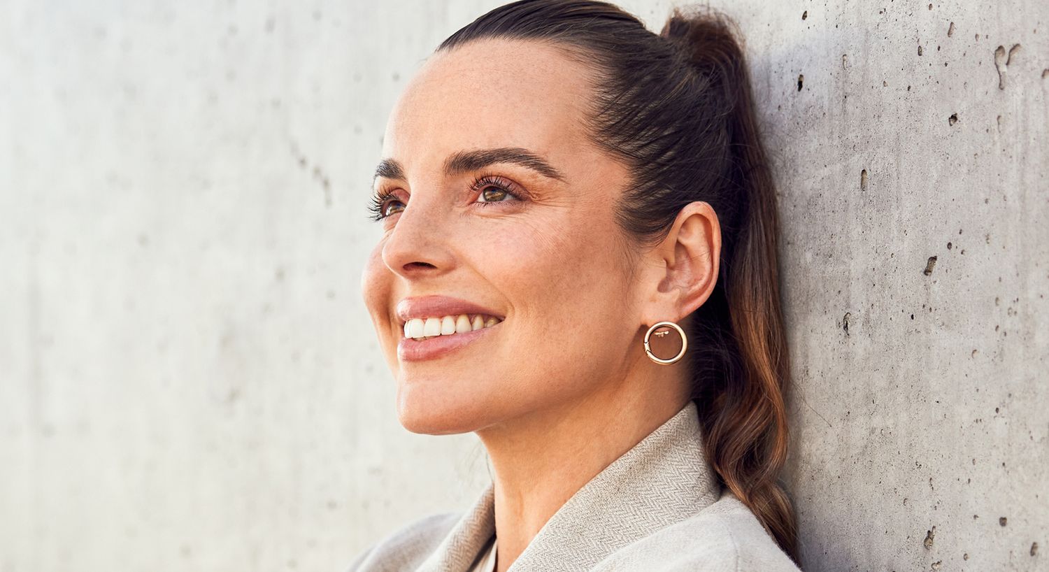 Woman smiling against a concrete wall background.